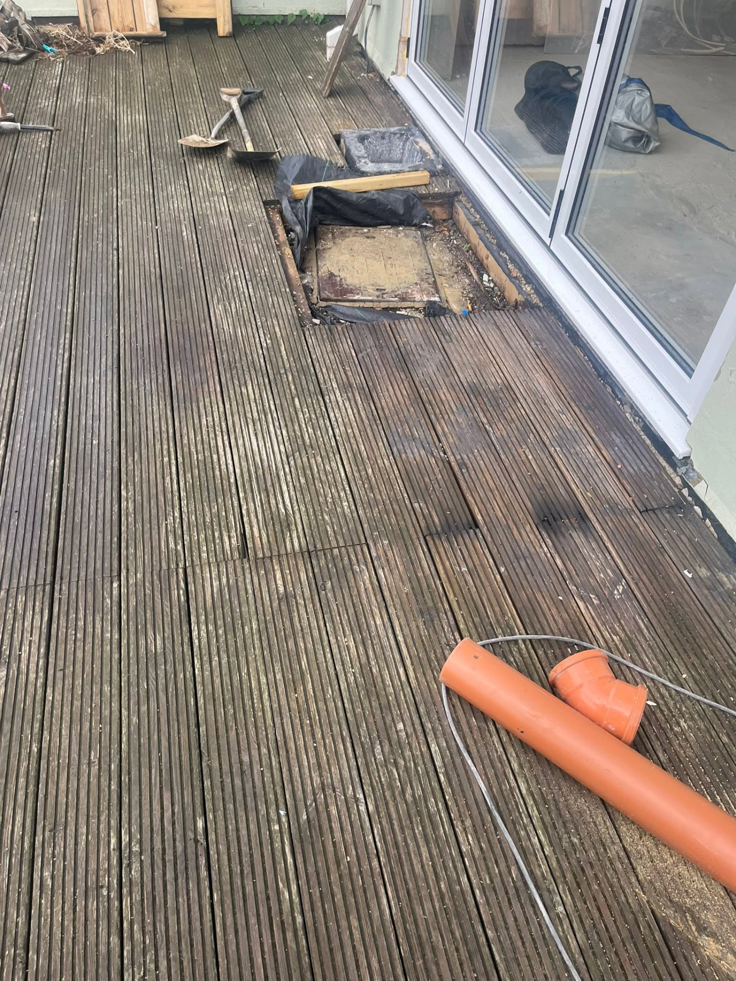 Decking lifted beside patio doors exposing the old drain cover before work starts