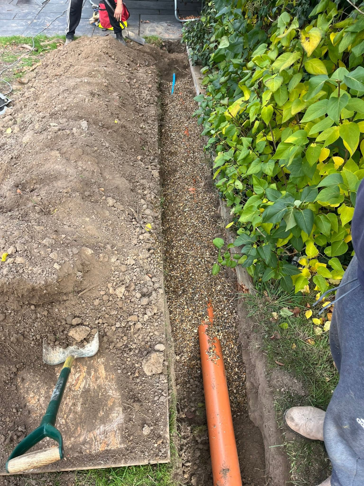 Orange underground drainage pipe bedded on pea shingle in the trench