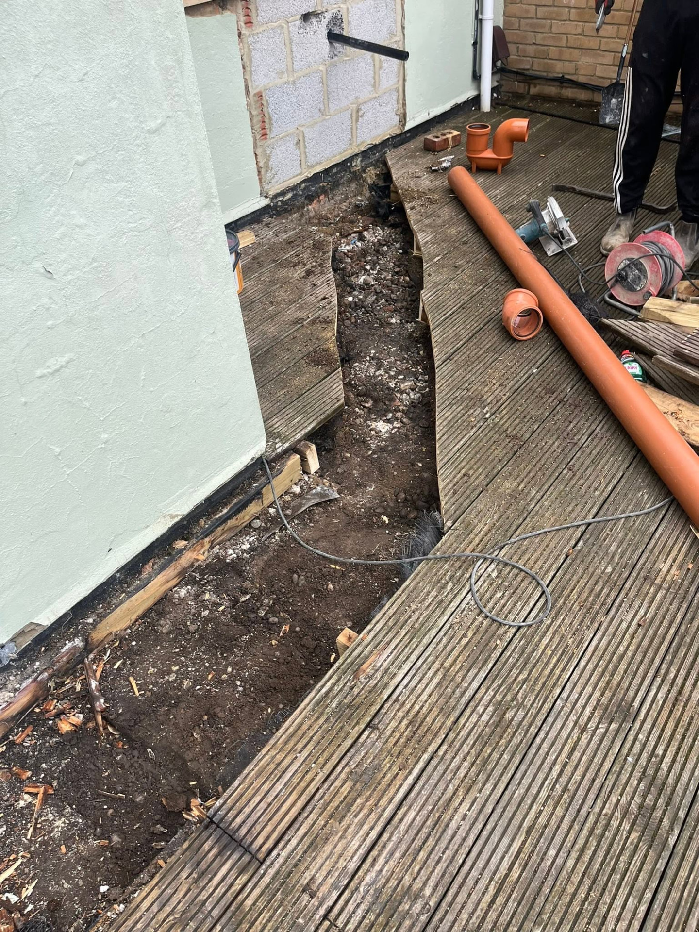 Trench dug along the wall with new orange pipe and fittings ready to install