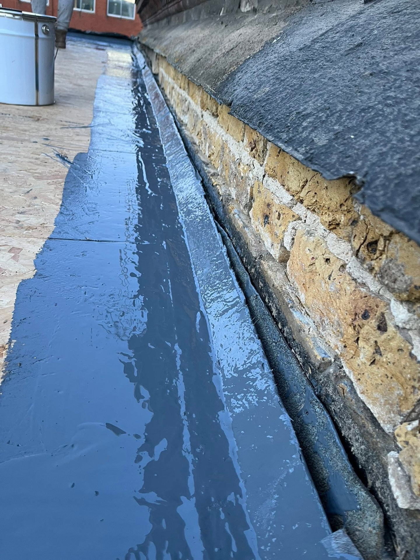 Liquid rubber coating being applied along the roof edge and upstand