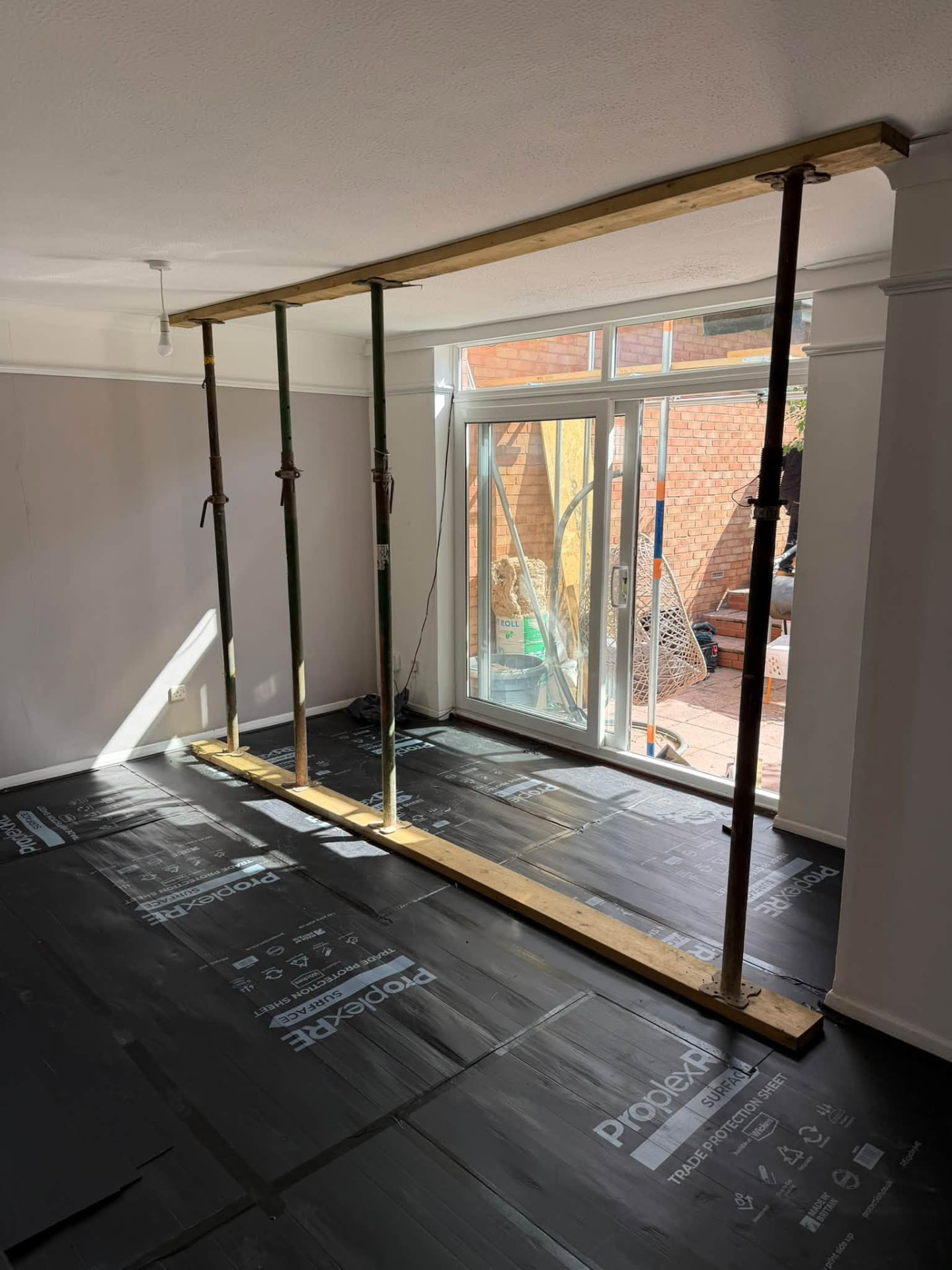 Room prepared for structural work with temporary props and floor protection sheets in place