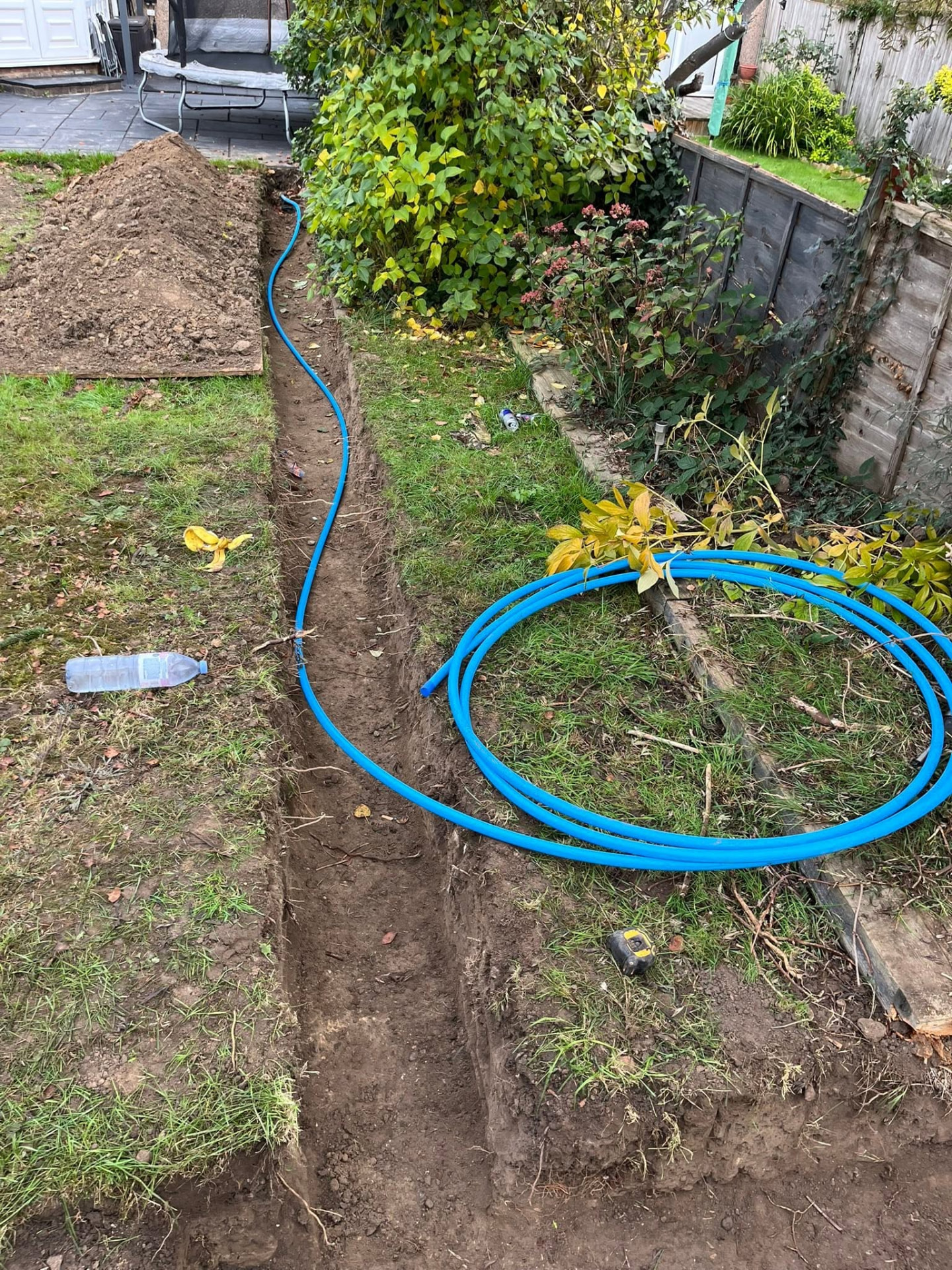 Coiled blue MDPE mains water pipe being fed into the trench run