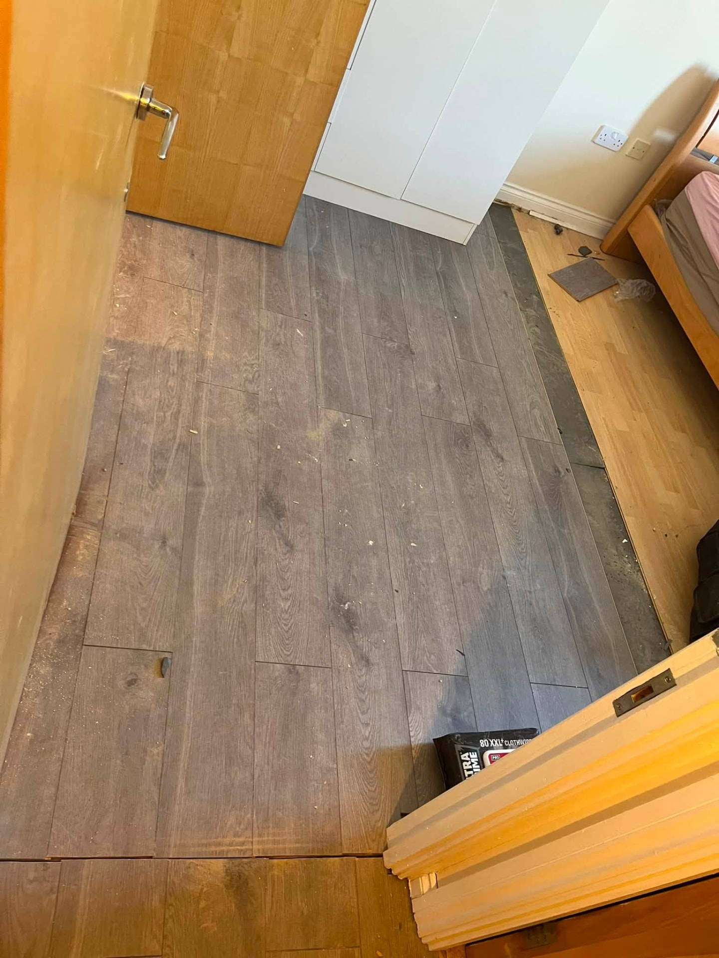 New grey oak laminate flooring being laid through the bedroom doorway