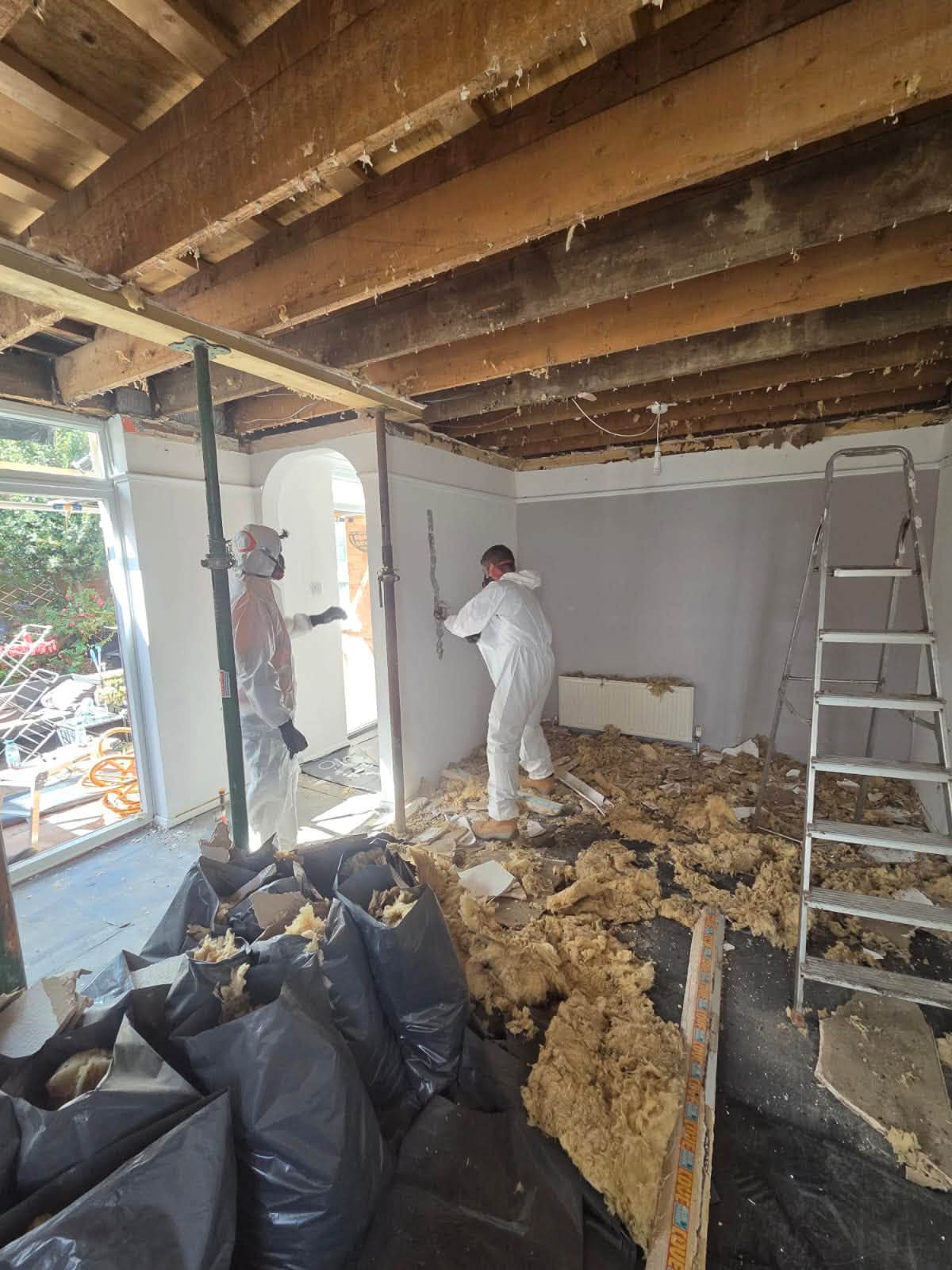 Two tradesmen in protective suits clearing old insulation from the room