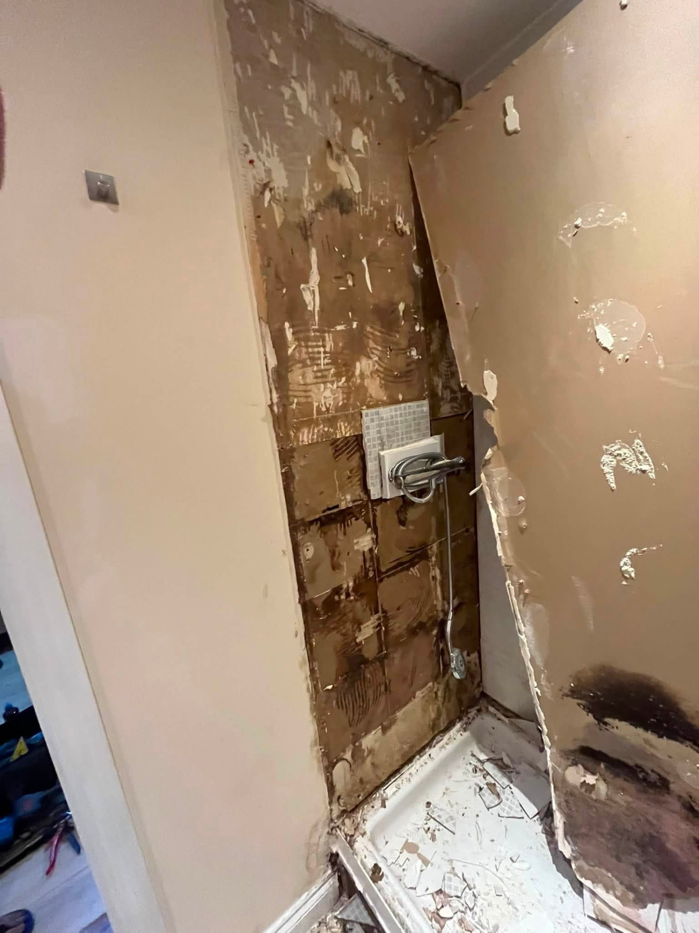 Tiles and boarding removed from the shower corner exposing the wall behind