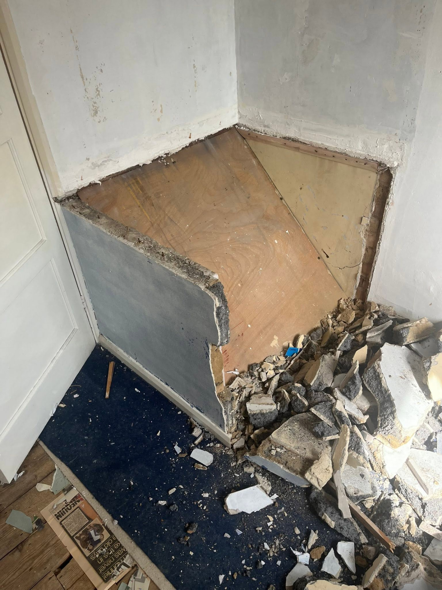 Old built-in cupboard stripped out with rubble and exposed plywood in the alcove