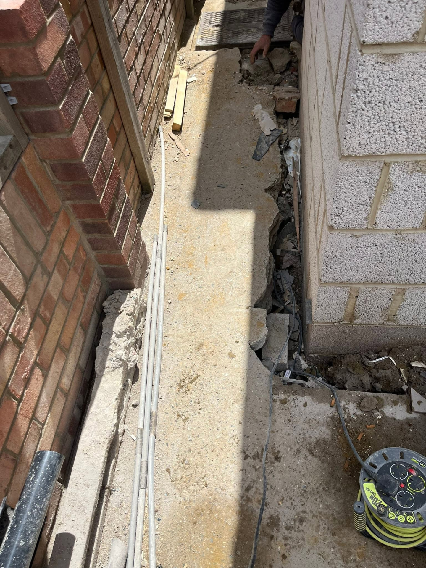 Narrow side passage with concrete path being broken out beside the existing drain cover