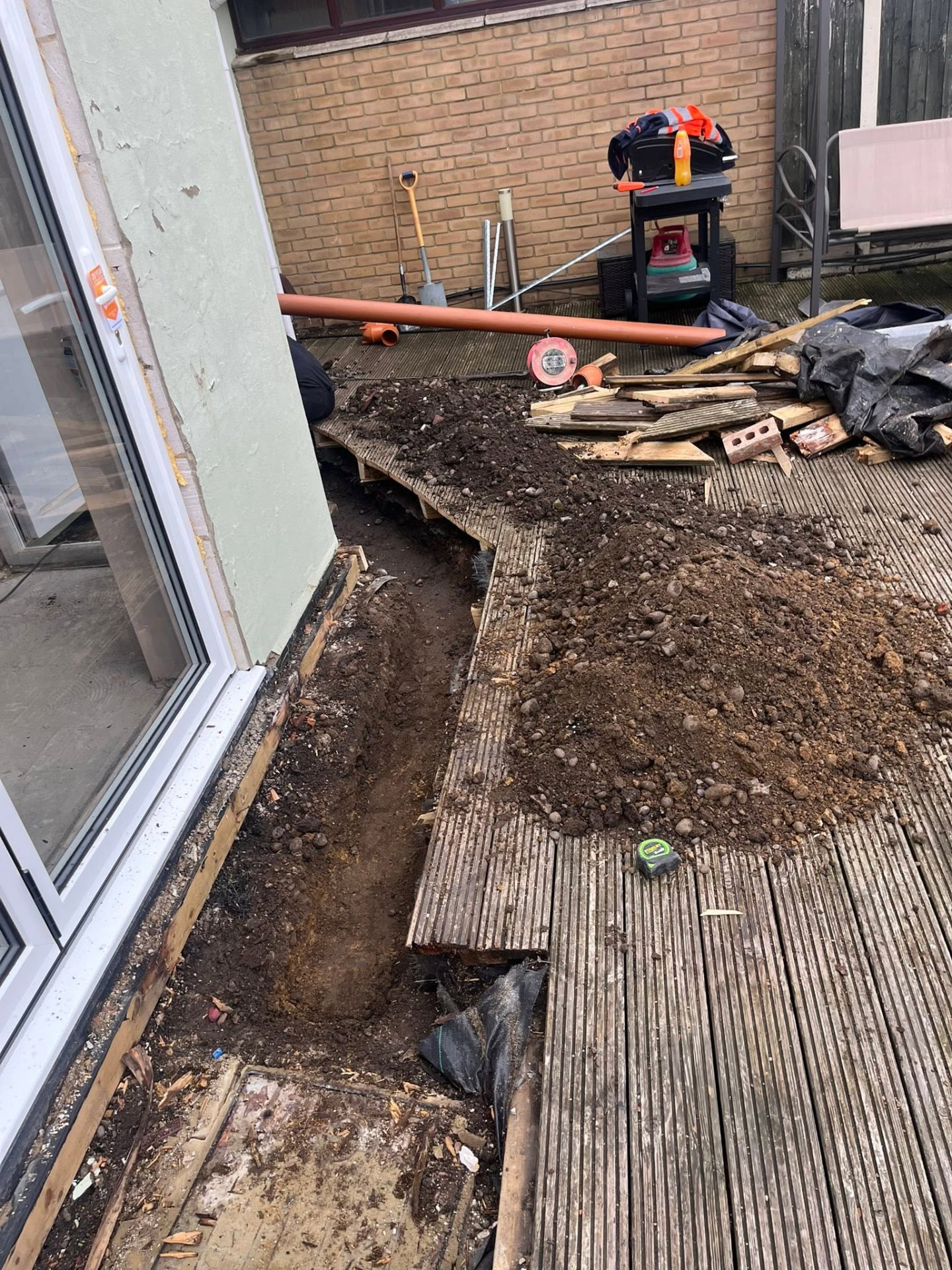 Excavated spoil on the decking as the drainage trench is extended along the property