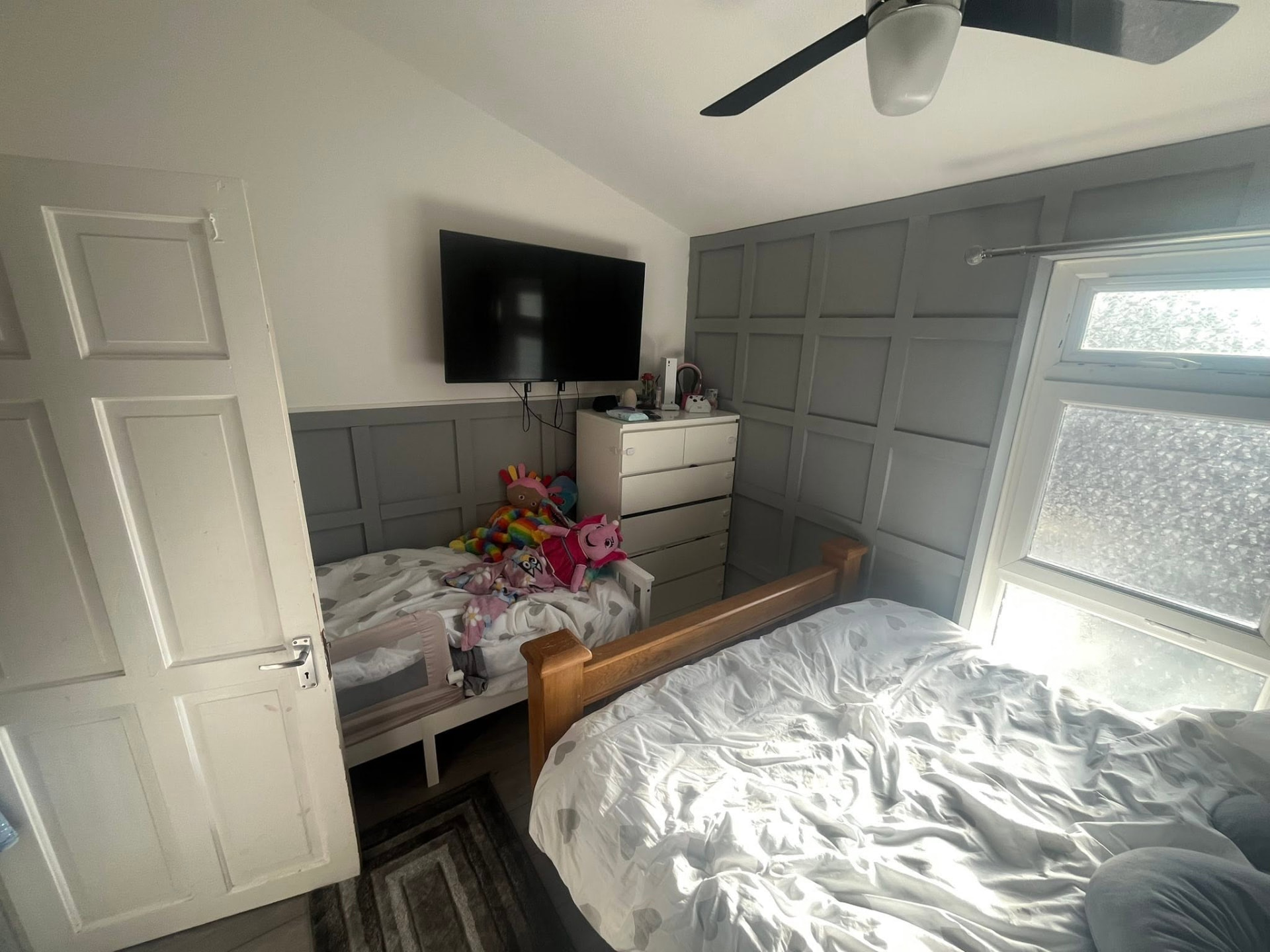 Finished bedroom with grey panelled walls, new flooring and wall-mounted TV