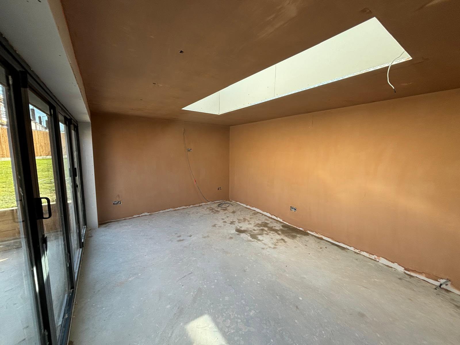 Newly skimmed open-plan room with smooth plaster finish and long roof lantern