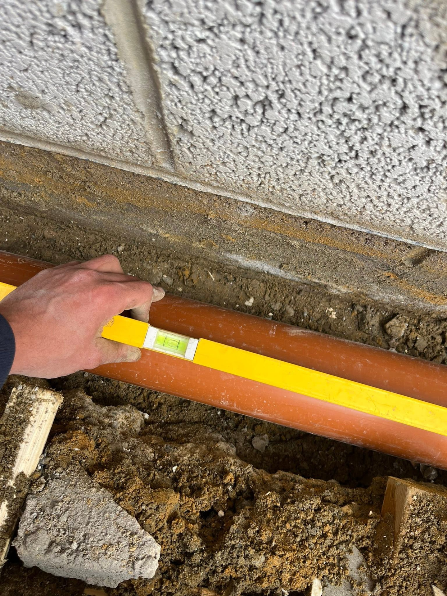 Spirit level used to check the fall on the new 4-inch pipe run against the wall